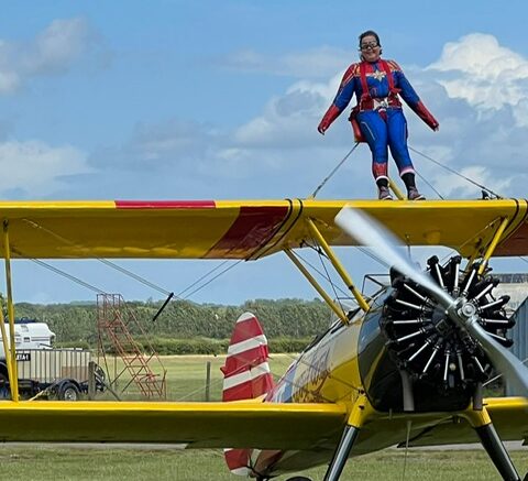 Harriet Bunn wing walking. Dress as Captain Marvel, strapped on top of a yellow biplane